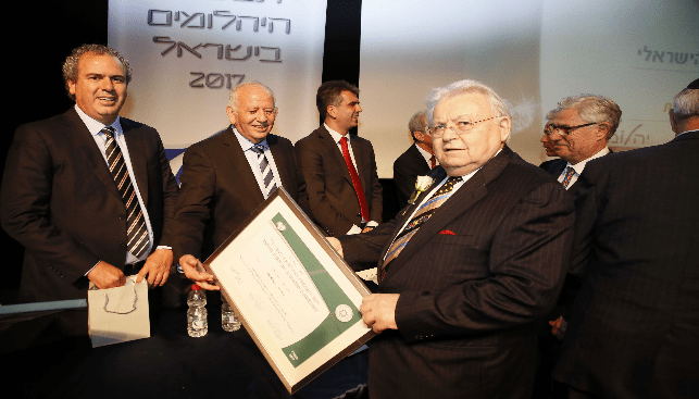 אריה ריגר מחזיק את תעודת יקיר תעשיית היהלומים אותה קיבל מנשיא בורסת היהלומים יורם דבש